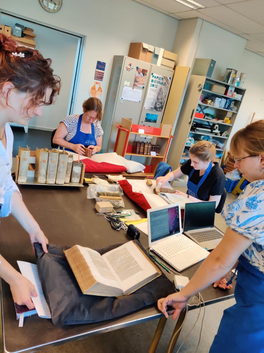 Diverse personen zijn over boeken en laptops gebogen die op een tafel staan