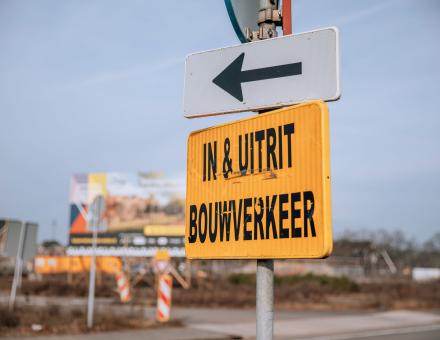 Geel bord met zwarte tekst 'in- en uitrit bouwverkeer'