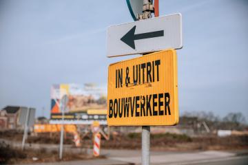 Geel bord met zwarte tekst 'in- en uitrit bouwverkeer'